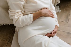 A serene moment of a pregnant woman in a cozy white dress holding her belly.